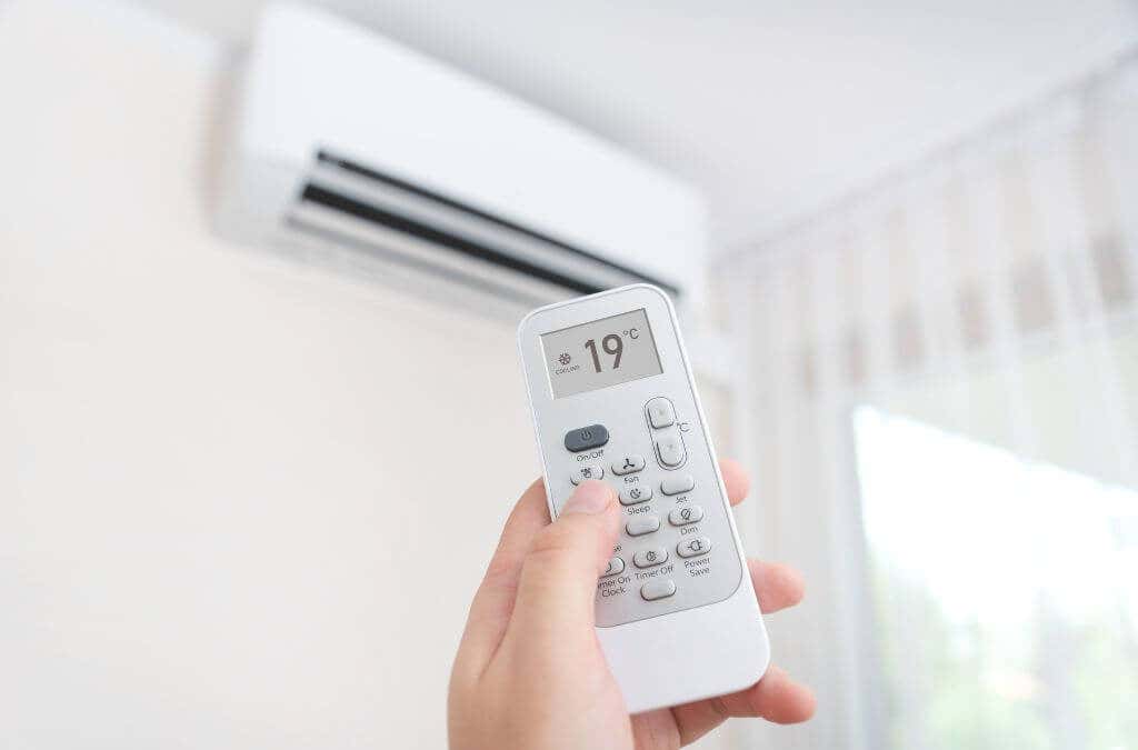 A hand holding up a remote control aimed at an air conditioning unit