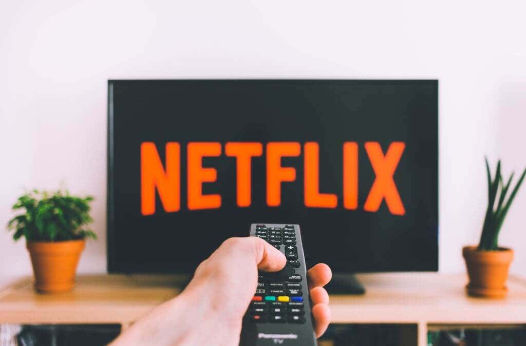 A hand holding a remote control aimed at a television screen with "NETFLIX" on-screen 