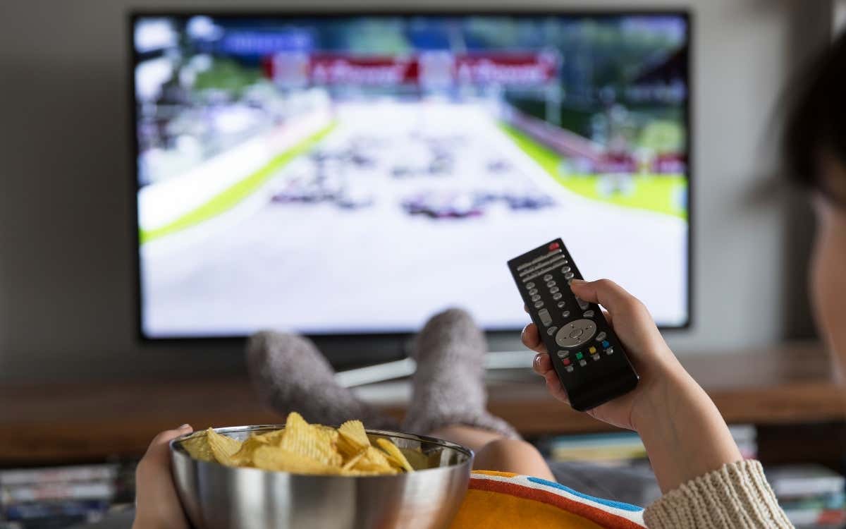 Person watching TV, holding a remote control and a bowl of chips