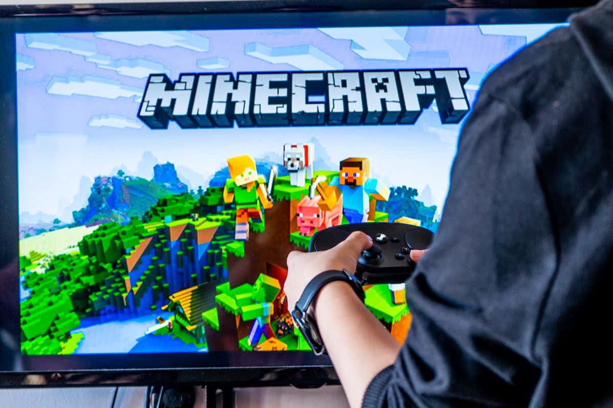  - Woman holding a steam controller and playing popular video game minecraft on a television and PC