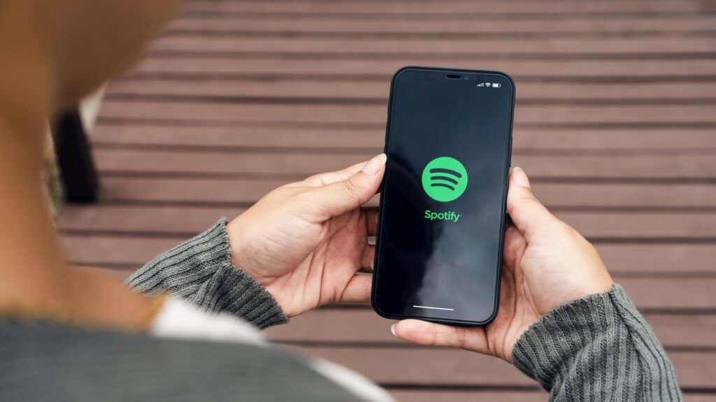 How to Block Someone on Spotify image - Girl in the park holding a smartphone with Spotify Music app on