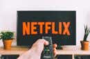 person holding a remote control pointed at a TV displaying the Netflix logo