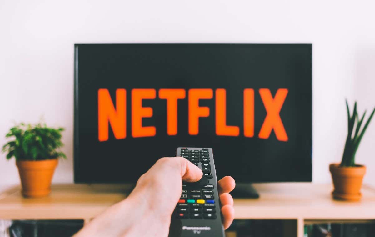 person holding a remote control pointed at a TV displaying the Netflix logo - a-person-holding-a-remote-control-pointed-at-a-TV-displaying-the-Netflix-logo