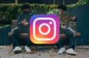 Two identical individuals sitting side-by-side on a bench with their faces obscured by a large Instagram logo icon - instagram-meta-ai-studio